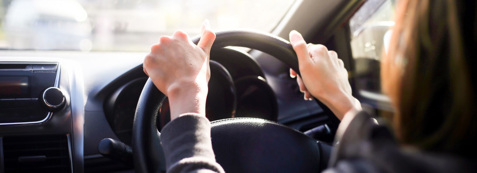 Fahrerin hält das Lenkrad während der Fahrt - Blick ins sonnendurchflutete Autoinnere.